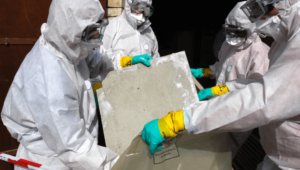 Two workers wearing masks and protective suits remove hazardous asbestos products